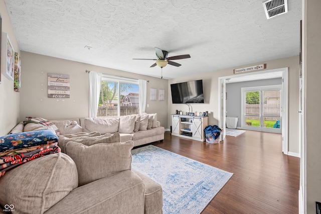 living area featuring healthy amount of natural light, a ceiling fan, wood finished floors, a textured ceiling, and baseboards
