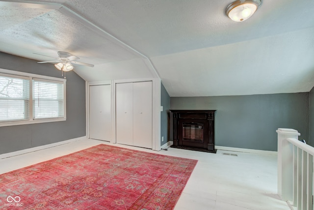 bonus room with vaulted ceiling, a textured ceiling, a ceiling fan, a fireplace with flush hearth, and baseboards