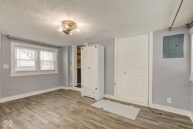 unfurnished bedroom with electric panel, wood finished floors, baseboards, a textured ceiling, and multiple closets