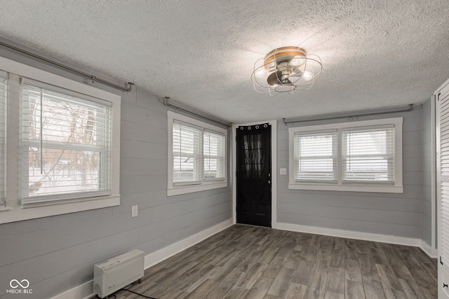 entrance foyer featuring a textured ceiling, dark wood-type flooring, baseboards, healthy amount of natural light, and wood walls