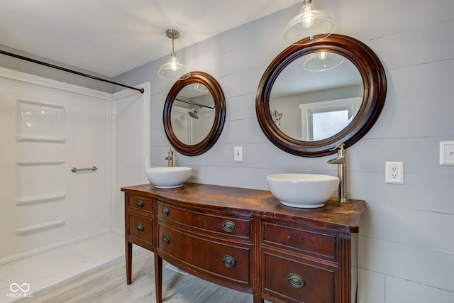 bathroom with a shower, double vanity, and wood finished floors