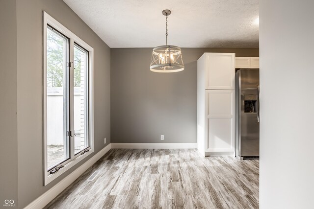 51 Glasgow Ln, Noblesville, IN 46060 - unfurnished dining area featuring light wood-type flooring, a chandelier, a textured ceiling, and baseboards