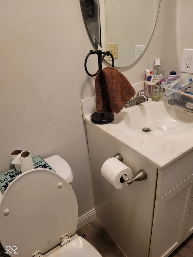 half bath with wood finished floors, toilet, vanity, and baseboards