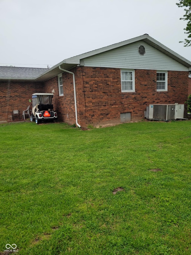 view of home's exterior with brick siding, a yard, and central AC