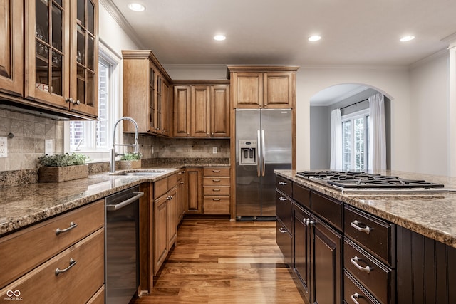 kitchen featuring stainless steel appliances, a sink, ornamental molding, arched walkways, and light wood-type flooring