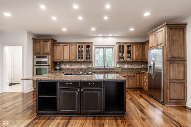 kitchen featuring stainless steel appliances, ornamental molding, a sink, open shelves, and a center island