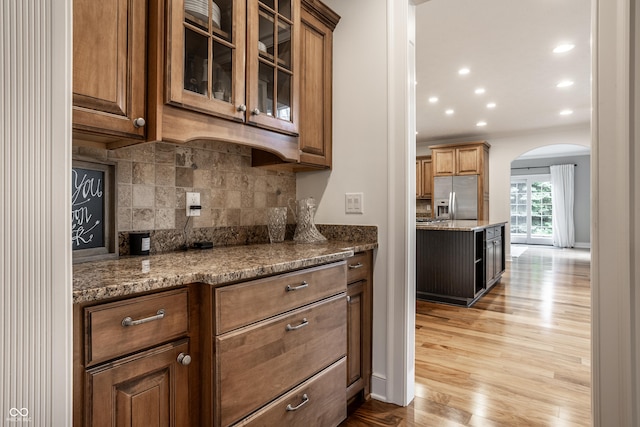 bar area featuring stainless steel fridge, arched walkways, light wood-type flooring, backsplash, and recessed lighting