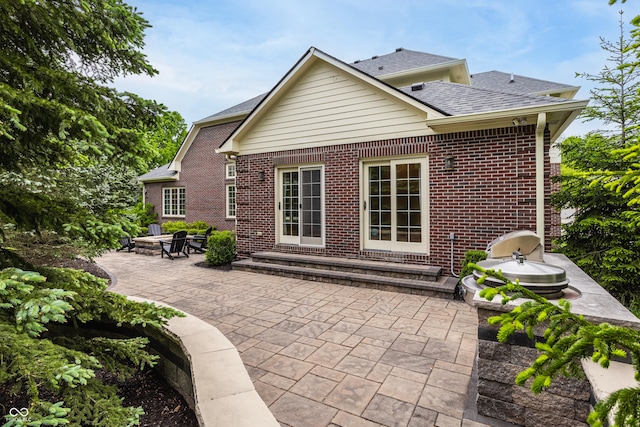 back of house featuring a patio, brick siding, a shingled roof, and an outdoor fire pit
