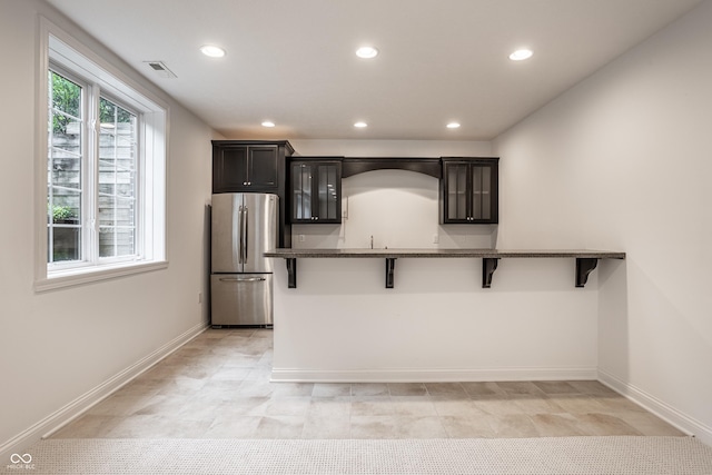 kitchen featuring freestanding refrigerator, a breakfast bar, recessed lighting, baseboards, and dark stone counters
