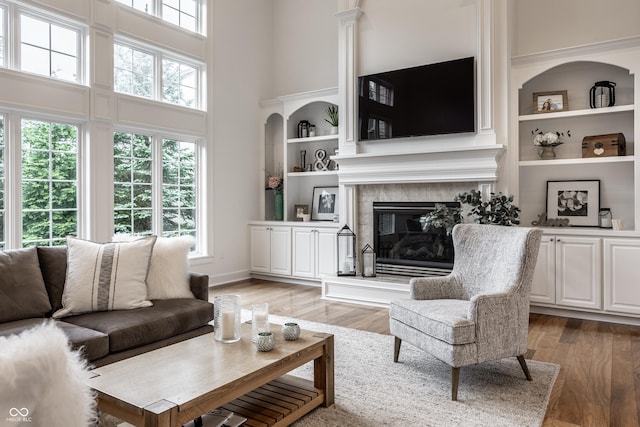 living area featuring a high ceiling, light wood-type flooring, a fireplace, and built in shelves