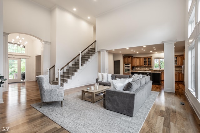 living area with a high ceiling, ornate columns, arched walkways, stairs, and wood finished floors