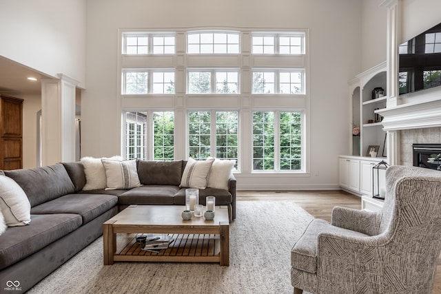 living area with a high ceiling, light wood-style floors, plenty of natural light, a glass covered fireplace, and baseboards