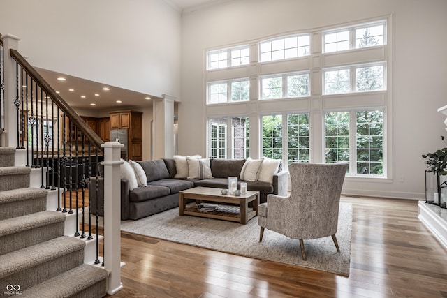 living area with a towering ceiling, wood-type flooring, stairway, crown molding, and baseboards