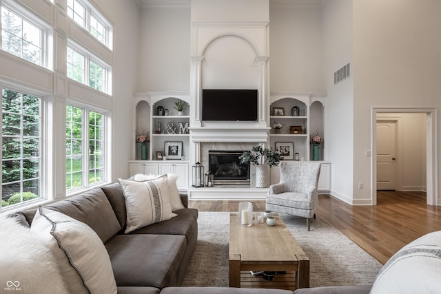 living area with a high ceiling, a glass covered fireplace, built in shelves, ornamental molding, and wood finished floors