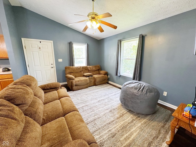 living room featuring a ceiling fan, lofted ceiling, healthy amount of natural light, baseboards, and a textured ceiling