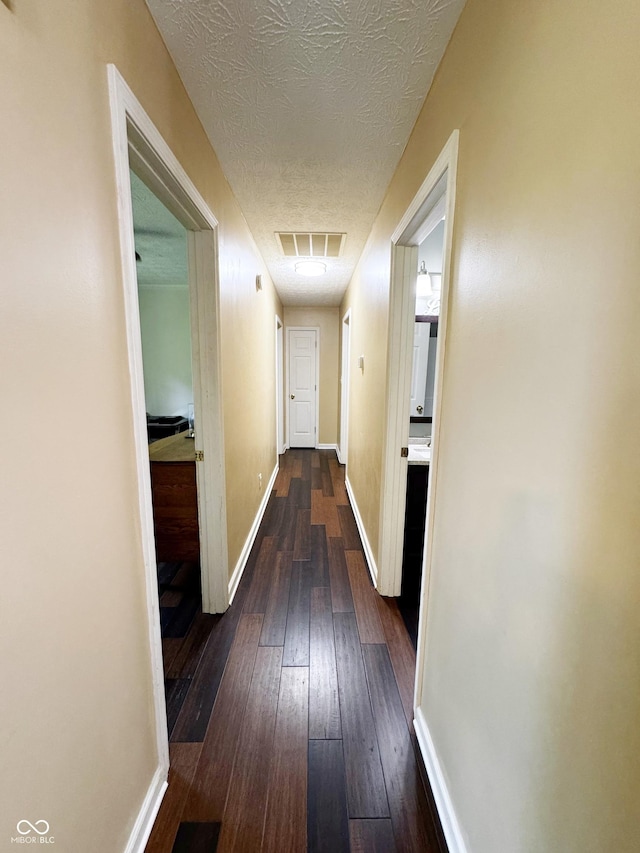 corridor with dark wood-type flooring, a textured ceiling, and baseboards