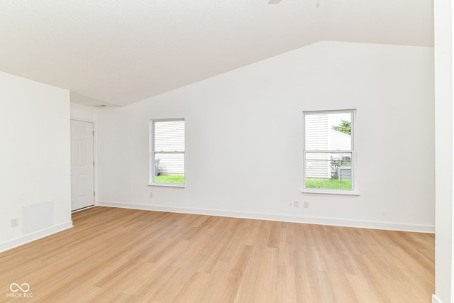 spare room with vaulted ceiling, light wood finished floors, plenty of natural light, and baseboards