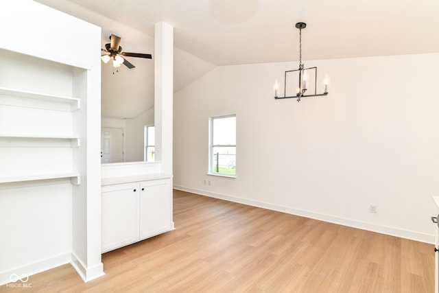 unfurnished dining area featuring light wood finished floors, a chandelier, a ceiling fan, baseboards, and vaulted ceiling