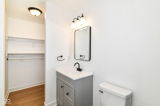 bathroom with wood finished floors, toilet, vanity, baseboards, and a spacious closet