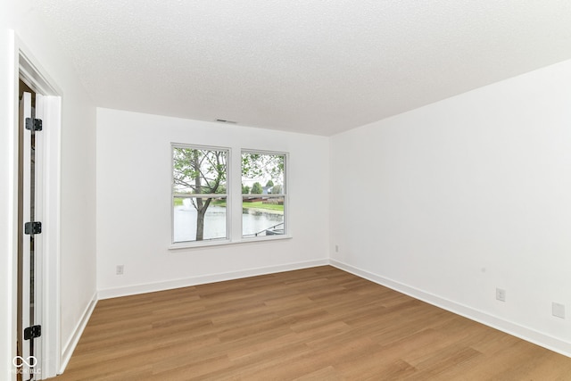 empty room featuring light wood-type flooring, baseboards, and a textured ceiling