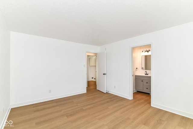 unfurnished bedroom featuring light wood finished floors, a sink, baseboards, and ensuite bath