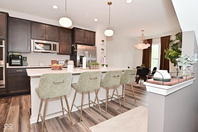3110 W New York St, Indianapolis, IN 46222 - kitchen featuring appliances with stainless steel finishes, wood finished floors, dark brown cabinetry, light countertops, and a kitchen breakfast bar