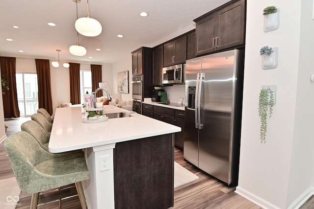 3110 W New York St, Indianapolis, IN 46222 - kitchen with stainless steel appliances, a sink, light wood finished floors, dark brown cabinetry, and an island with sink