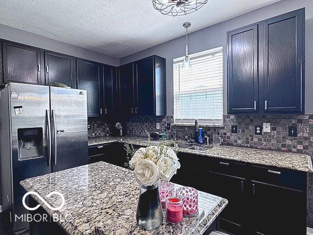 6155 W Bayfront, Mccordsville, IN 46055 - kitchen featuring stainless steel fridge with ice dispenser, backsplash, pendant lighting, light stone counters, and dark cabinetry