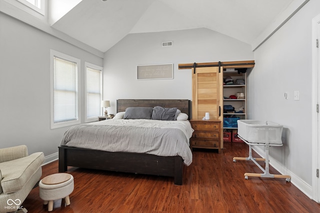 bedroom with a barn door, multiple windows, a walk in closet, wood finished floors, and lofted ceiling