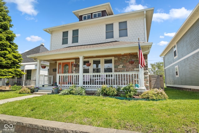 traditional style home featuring a porch, a front lawn, stone siding, and a shingled roof