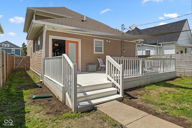 rear view of property featuring a wooden deck, roof with shingles, and a fenced backyard