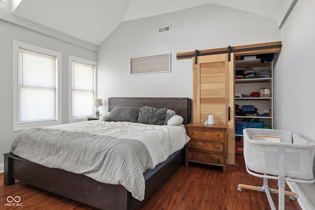 bedroom featuring vaulted ceiling, a spacious closet, a barn door, wood finished floors, and a closet