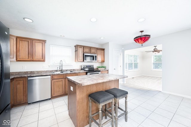kitchen featuring appliances with stainless steel finishes, a sink, a kitchen island, a kitchen bar, and light tile patterned floors