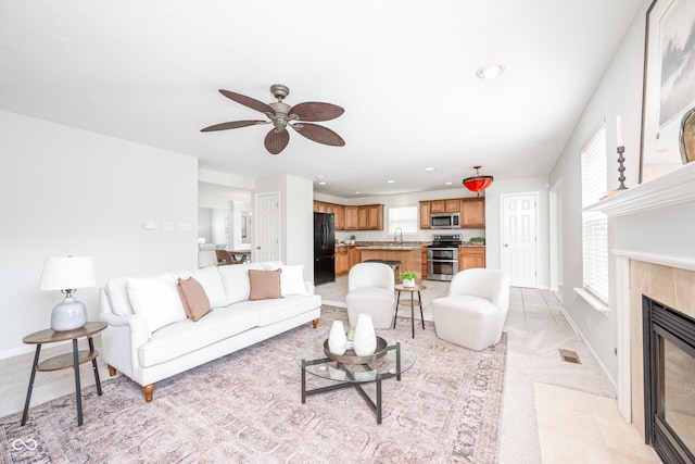 living room featuring a ceiling fan, a tiled fireplace, baseboards, light carpet, and recessed lighting