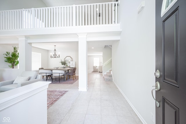 entryway featuring light tile patterned floors, stairs, a towering ceiling, a chandelier, and decorative columns