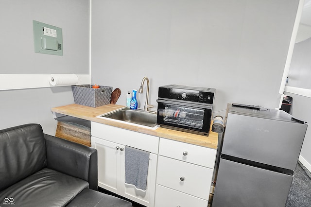 kitchen with a sink, white cabinetry, freestanding refrigerator, and wooden counters