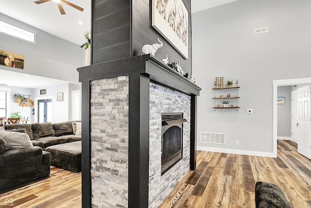 living room with a high ceiling, a ceiling fan, a fireplace, wood finished floors, and baseboards