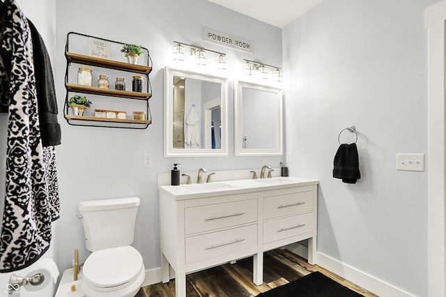 bathroom with toilet, wood finished floors, double vanity, and baseboards