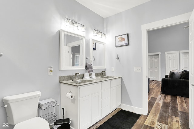 bathroom featuring wood finished floors, toilet, double vanity, and baseboards
