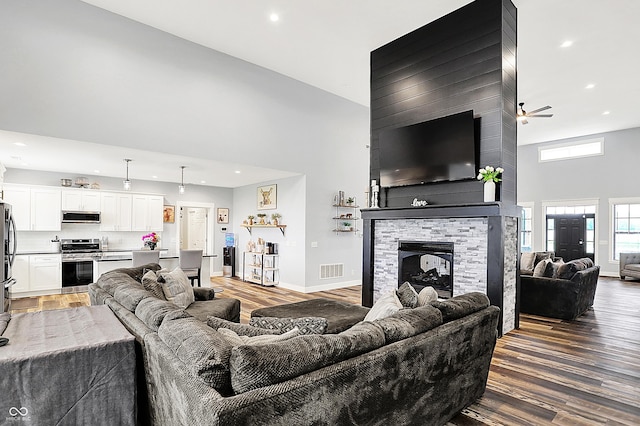living area with a towering ceiling, recessed lighting, wood finished floors, a fireplace, and baseboards