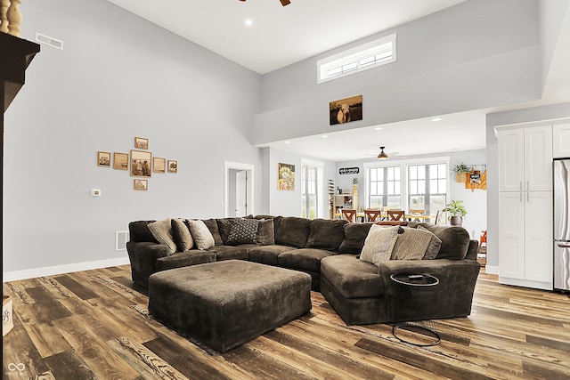 living room with ceiling fan, wood finished floors, a towering ceiling, baseboards, and recessed lighting