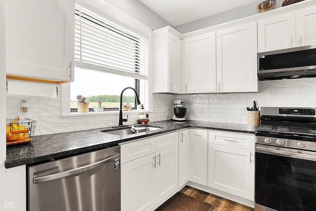 kitchen featuring appliances with stainless steel finishes, a sink, white cabinetry, backsplash, and dark stone countertops