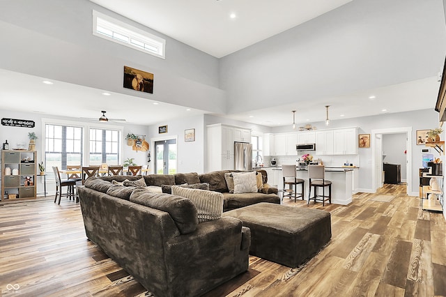 living area featuring light wood-type flooring, a ceiling fan, a towering ceiling, and recessed lighting