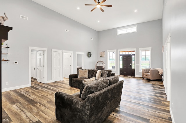 living area with a towering ceiling, a ceiling fan, baseboards, wood finished floors, and recessed lighting