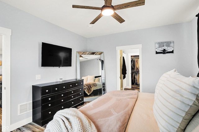 bedroom with a spacious closet, a closet, a ceiling fan, and wood finished floors