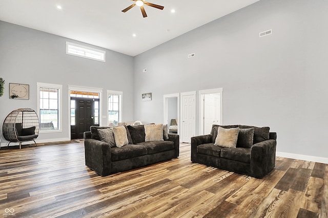 living area with a ceiling fan, a high ceiling, wood finished floors, baseboards, and recessed lighting