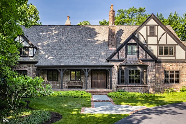 7406 N Washington Blvd, Indianapolis, IN 46240 - tudor house featuring brick siding, a front lawn, a chimney, covered porch, and a shingled roof