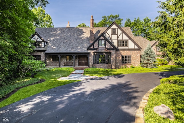7406 N Washington Blvd, Indianapolis, IN 46240 - tudor-style house featuring a porch, brick siding, a front yard, a chimney, and stucco siding