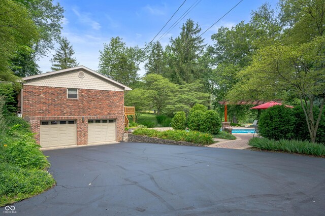 17216 W Hunnicut Rd, Cambridge City, IN 47327 - view of side of home with driveway, brick siding, an attached garage, and an outdoor pool