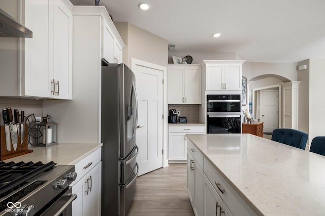 3622 S Setting Sun Ln, New Palestine, IN 46163 - kitchen featuring appliances with stainless steel finishes, arched walkways, tasteful backsplash, light wood-type flooring, and wall chimney range hood